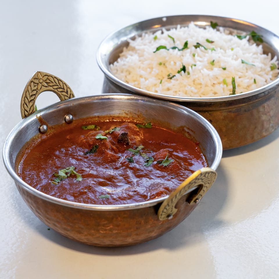 Copper serving bowls hold rich red curry garnished with cilantro and fluffy white rice on a restaurant table.