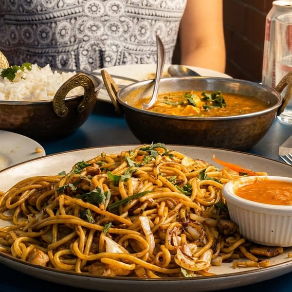 A vibrant spread of Indo-Chinese and Indian dishes, including noodles, rice, and curry, on a blue table.
