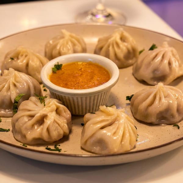 Plate of steamed momos with a small bowl of orange dipping sauce, garnished with herbs.