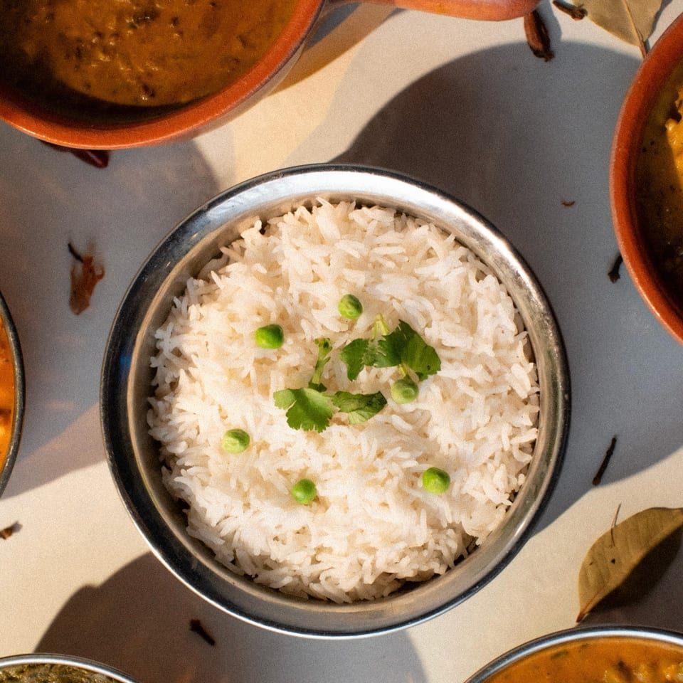 Overhead view of a bowl of white rice with peas and cilantro, surrounded by other Indian dishes.