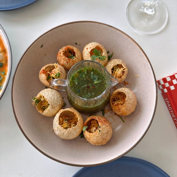 A plate of crispy pani puri shells filled with ingredients, surrounding a pitcher of green pani.