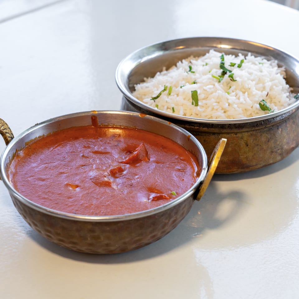Copper serving bowls hold creamy red curry and fragrant white rice garnished with fresh herbs on a restaurant table.
